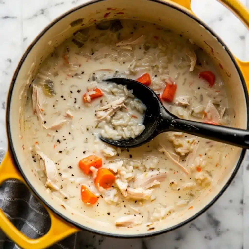 Creamy Chicken and Rice Soup: A Comfort Food Classic 9 A yellow Dutch oven filled with creamy chicken and rice soup, featuring shredded chicken, carrots, celery, and black pepper, with a black ladle.