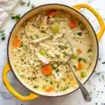 Creamy Chicken and Rice Soup: A Comfort Food Classic 11 A pot of creamy chicken and rice soup with shredded chicken, carrots, peas, celery, and fresh herbs, served in a yellow Dutch oven with a silver ladle.